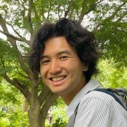 A person smiling at the camera with a tree behind them